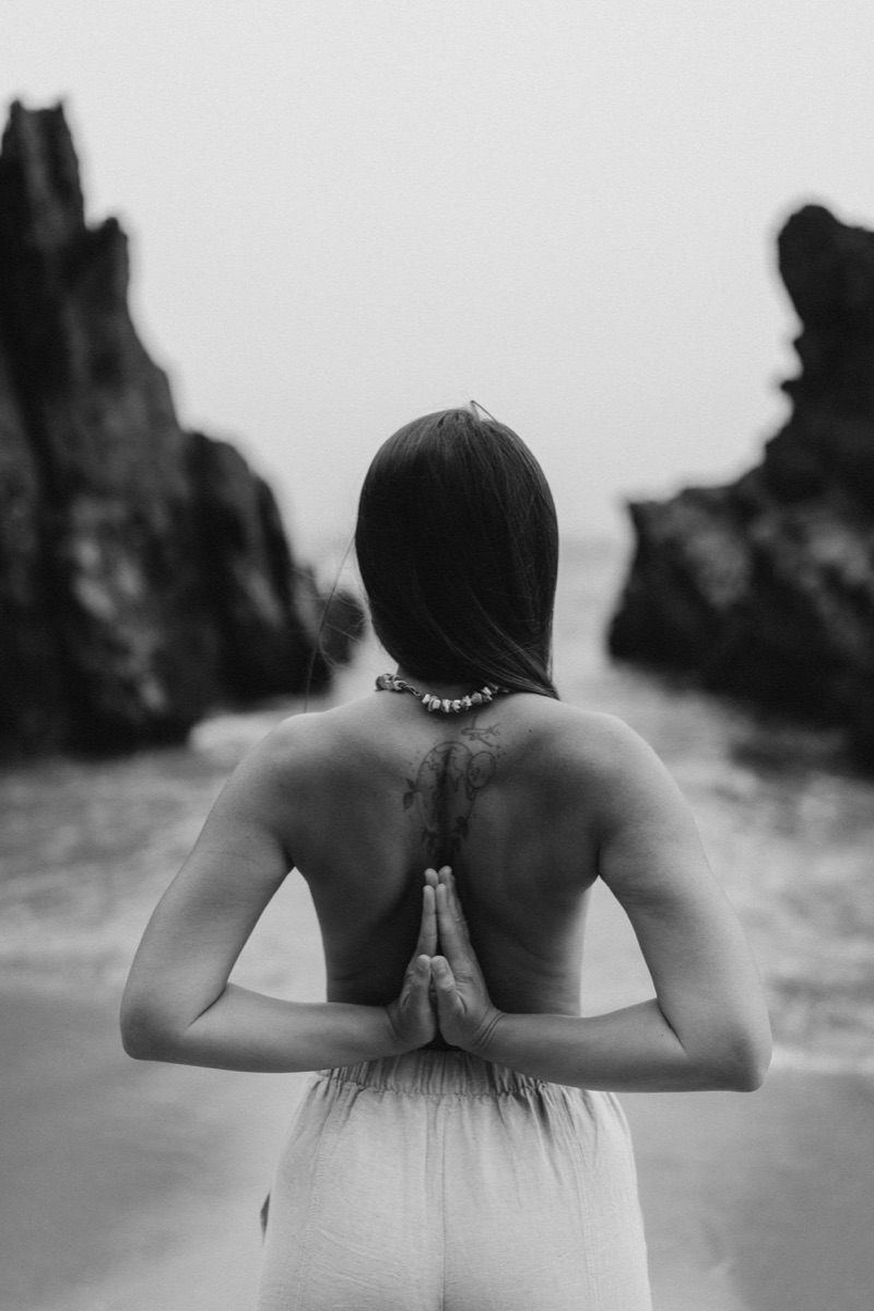 Woman in reverse prayer yoga pose on a beach between rock formations