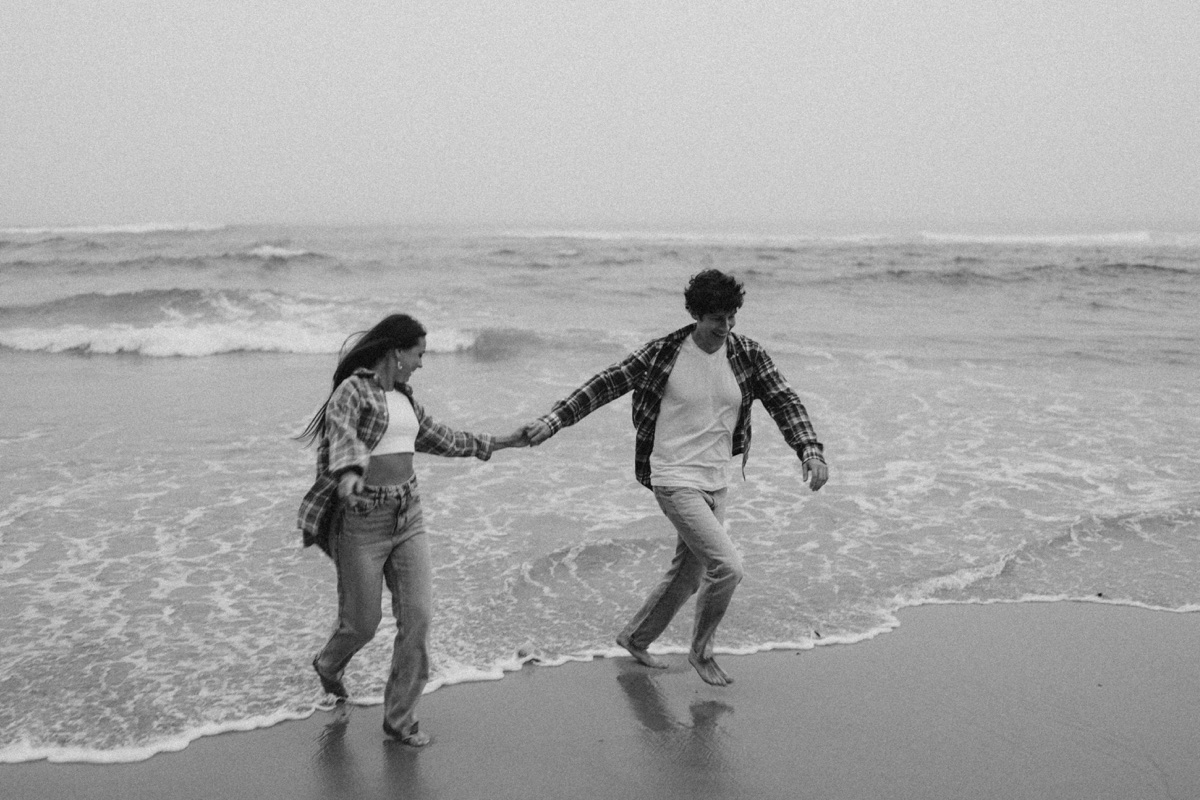 Couple running hand in hand along the shoreline, black and white